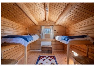 Fotografi av en innredet hytte eller soverom med senger, gulv og tak i tre.