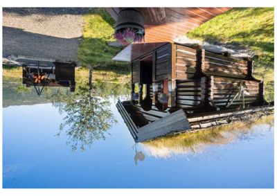 Fotografi av en ferdigbygd hytte med grønt tak, utsikt over fjell og en ildsted i bakgrunnen.