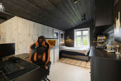 Fotografi av et innredet soverom med mørke trepaneler på vegger og tak, en gaming-stol, en seng og et skrivebord.