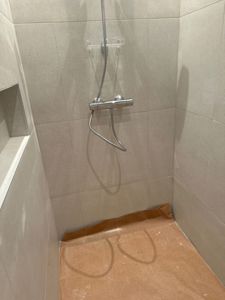 Fotografi av en nybygd dusj med fliser og dusjhode.