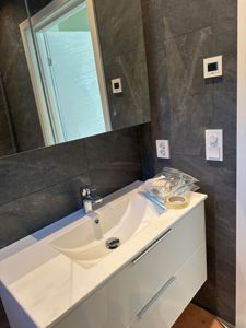 Fotografi av en innredet badromsvask med speil, veggfliser og utstyr på benken.