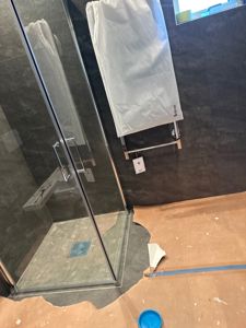 Fotografi av en badedusj med glassdør og mørke fliser under renovering.