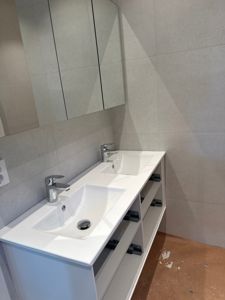 Fotografi av et innredet bad med dobbeltvask, speilskap og flisvegger.