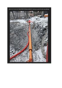 Fotografi av en graving på byggeplass med en person som arbeider med å legge eller justere en stor oransje rørledning i et grøft.