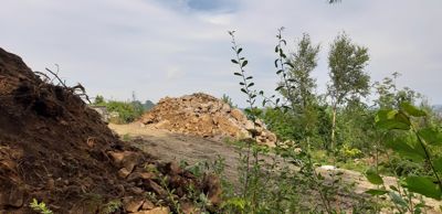 Fotografi av et byggeområde med en stor haug med grus eller stein i bakgrunnen, omgitt av vegetasjon.
