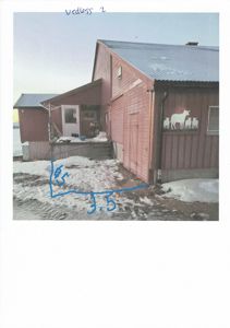 Fotografi av en rød, langbygget bygning (muligens en uthus eller garasje) med et blått tak. Bygningen har et hvitt døråpning, vinduer og et dekorativt motiv av dyr på veggen. Det er snø på bakken, og det er håndskrevne notater ("Vedloss 2" og mål "18" og "3.5") på bildet.