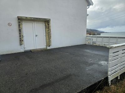 Fotografi av en hvit fasade med en dobbeltdør og en betongterrasse med hvit hekk.