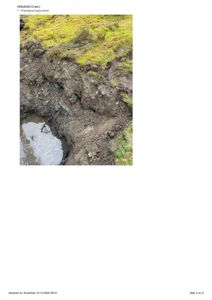 Fotografi av en prøvegraving i jorda, med synlig grus, mudder og vann i bunnen.