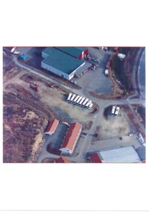 Flyfoto eller luftfoto som viser et område med flere bygninger, parkeringsplasser og veier.