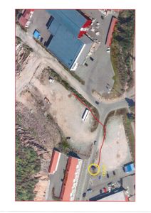 Flyfoto eller satellittbilde av et område med bygninger, veier og tomter, med en rød linje som markerer en grense eller vei.