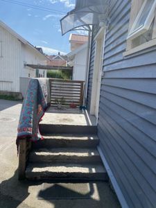 Fotografi av en trapp opp til en inngang med en veranda, sett fra bakkenivå.