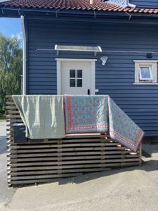 Fotografi av en blå hytte med hvit dør og vindu, sett fra foran. Det er en pall med klær hengt opp foran huset.