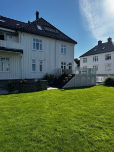 Fotografi av en hvit, trepanelert villa med grønn hage og en tilstøtende bygning.