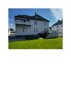 Fotografi av en hvit, toetasje villa med mørkt tak sett fra bakgården.