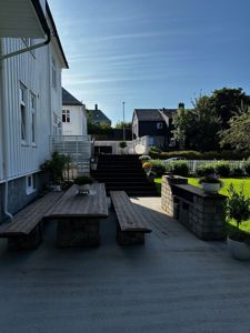 Fotografi av en uteplass med bord, benker og trapper foran en hvit bygning.