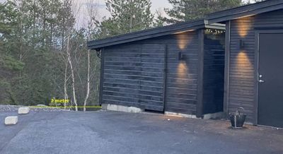 Fotografi av en mørk, moderne bygning (garasje eller uthus) med en markert avstand på 2 meter til en grense.