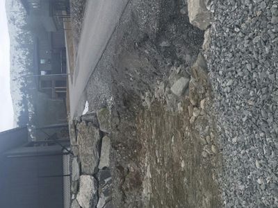 Fotografi av en byggeplass eller tomt med steinmur, grus og asfaltert vei.