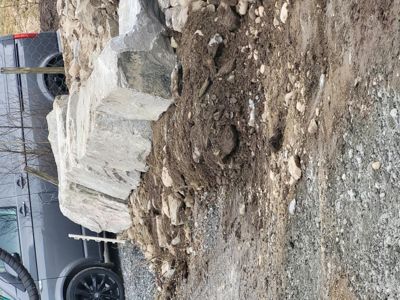 Fotografi av en byggeplass eller graving, med en bil og steinblokker i forgrunnen.