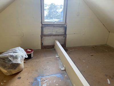 Fotografi av et utbyggingsrom (sannsynligvis etasjehøy) med skrå tak, en vindusåpning og en delvis oppstilt innvendig vegg.