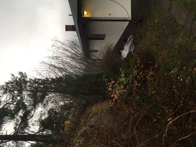 Fotografi av en bygning sett fra siden, med omgivende vegetasjon og himmel.