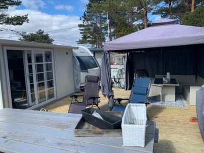 Fotografi av en uteområde med en hytte, en campingvogn, en terrasse med møbler og en solseil.