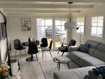 Fotografi av et innvendig rom (stue/spisestue) med møbler, vinduer og gulv.