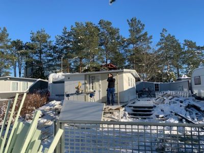 Fotografi av en hvit containerhytte eller modulbygg i en snødekket hage med en person som står på en plattform foran bygningen.