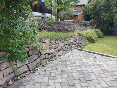 Fotografi av en utvendig hage- og veioppgradering med steinmur og asfaltert vei.