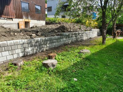 Fotografi av en byggeplass med en ny mur, en del av en bygning og trær.