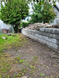 Fotografi av en pågående bygge- eller anleggsarbeid på en tomt, med en ny mur av betongblokker i forgrunnen.