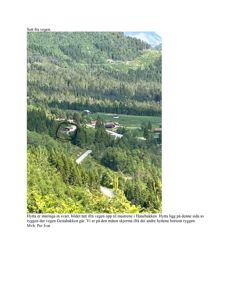 Fotografi av en hytte sett fra veien opp til mastrene i Hanebakken, med omgivende natur og andre hytter i bakgrunnen.