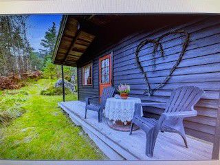 Fotografi av en hytte med en liten veranda, møbler og et hjerte laget av grener på veggen.