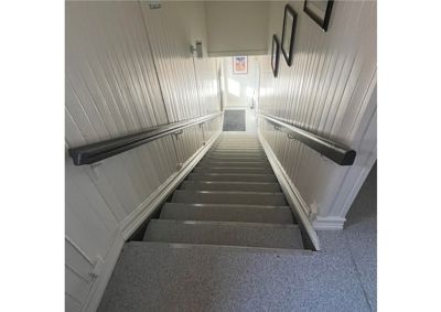 Fotografi av en trapp med håndtak og hvite panelvegger.