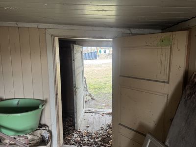 Fotografi av en døråpning i en bygning, med utsikt ut til en hage og søppelcontainere.