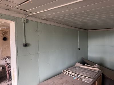 Fotografi av et roms indre med grønnmalt gipsvegg, hvit takpaneling og synlig elektrisk ledning.