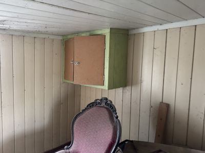 Fotografi av et rom med panelvegger, hvit taklist og en grønn skap med to dører. En stol er synlig i forgrunnen.