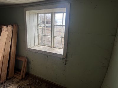 Fotografi av et rom inne i en bygning, med fokus på en vindu og en vegg med grønn maling. Det er også synlig at det ligger byggematerialer (treplater) i hjørnet.