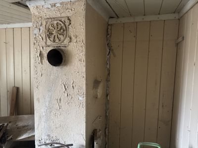 Fotografi av en innvendig vegg eller hjørne i en bygning, som viser en dekorativ, skadet søyle med et runde hull og en relieffskulptur.