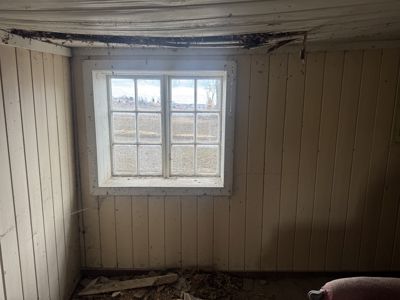 Fotografi av et roms indre med panelvegger, et vindu og skader på takkonstruksjonen.