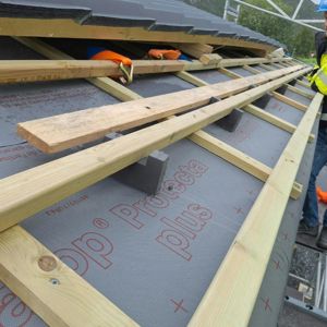 Fotografi av en takkonstruksjon under bygging, med synlig takbelegg, takbjelker og takpapir.