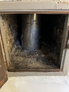 Fotografi av en metallrørledning (sannsynligvis ventilasjon eller røykledning) som er plassert i en utskjæring i en betong- eller murvegg.