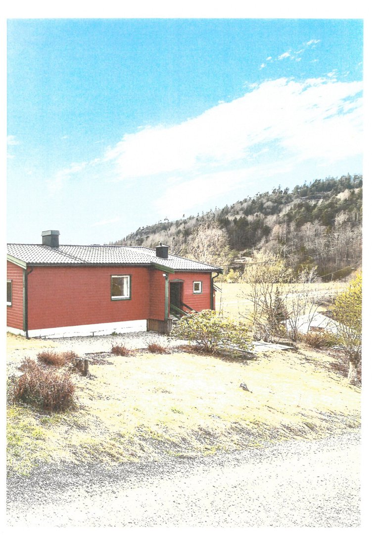 Fotografi av en rød enebolig sett fra siden, med en skogkledde bakke i bakgrunnen.