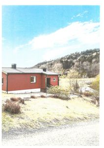 Fotografi av en rød enebolig sett fra siden, med en skogkledde bakke i bakgrunnen.