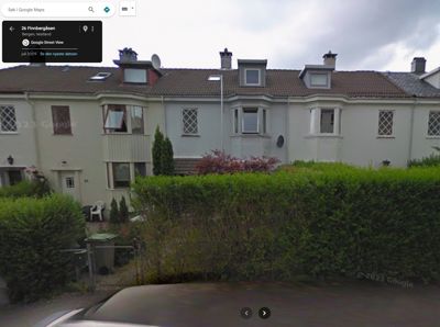 Fotografi av en rekkehusbebyggelse sett fra gaten, inkludert hager og fortau.