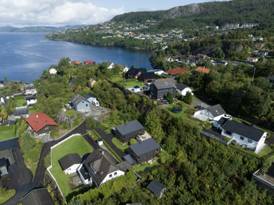 Luftfoto av et boligområde langs en kystlinje med fjell i bakgrunnen.
