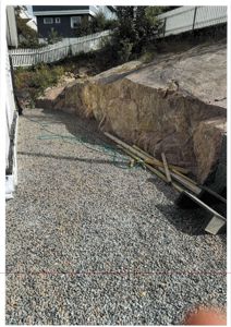 Fotografi av en byggeplass eller utvendig område med grus, en steil fjellside og en hvit hekk.