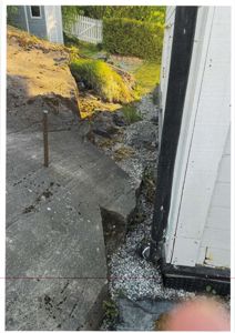 Fotografi av en utvendig byggeplass eller eksisterende bygning, som viser en betongplate, grus, og en del av en hvit bygning.