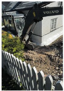 Fotografi av en byggeplass med en Volvo-graver som jobber ved siden av en eksisterende hvit bygning.