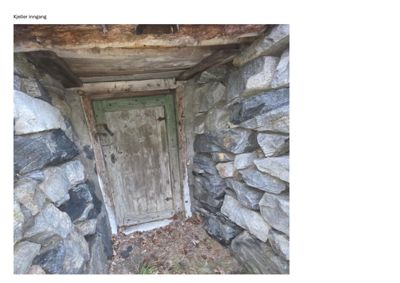 Fotografi av en gammel steinmur med en grønn dør, merket 'Kjeller inngang'.