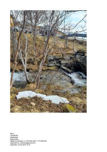 Fotografi av en bekke eller liten elv med en steinbro, snøflekker og trær i forgrunnen. I bakgrunnen er det synlig en vei og en bro.